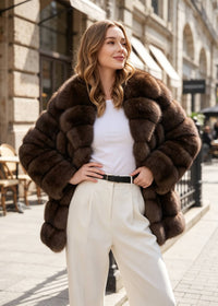 Front view of a woman with hands on hips showcasing a voluminous brown tiered wing-collar faux fur coat outdoors