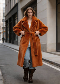 Front view of a model adjusting the waist belt on a rust brown long faux rabbit fur coat.