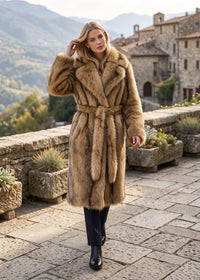 Outdoor full-body view of a model walking in an elegant camel brown longline faux fur coat cinched with a matching fur belt.