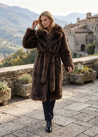 Blonde model walking in a dark brown longline faux fur wrap coat tied with a matching furry belt.
