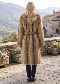 Back view of a woman wearing a camel brown belted faux fur longline wrap coat on an outdoor stone terrace.