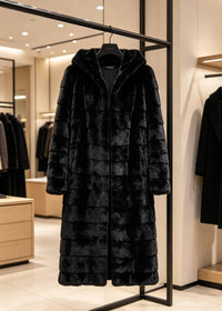 A long black faux fur coat with a tiered, quilted pattern and a hood, hanging on a black clothing rack inside a modern boutique.