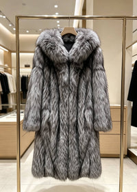 Women's silver-gray fox faux-fur longline hooded coat hanging on a wooden hanger on a gold display rack inside a showroom.