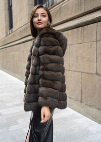 A profile shot of a woman smiling and looking slightly upward while wearing a plush, dark brown fur coat and a black leather skirt.