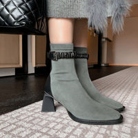 A woman wearing the grey suede ankle boots, showcasing the fit around the calf and the architectural block heel. They are paired with a grey knit skirt.
