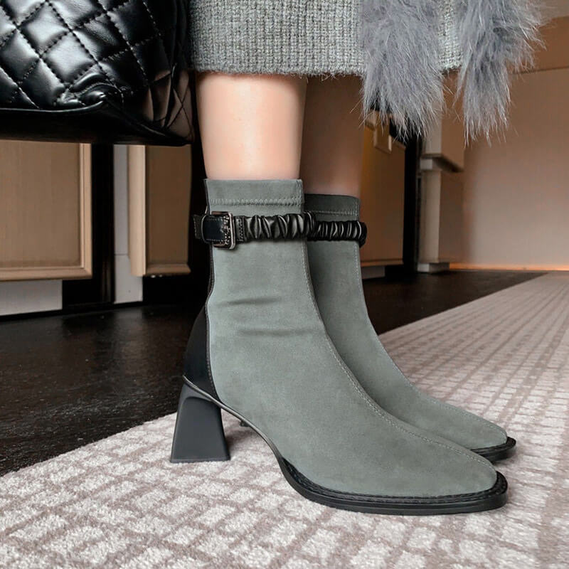 A woman wearing the grey suede ankle boots, showcasing the fit around the calf and the architectural block heel. They are paired with a grey knit skirt.
