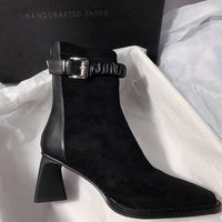 A profile shot of the black version of the ankle boot, showcasing the same buckled ruched strap and flared heel in an all-black colorway.