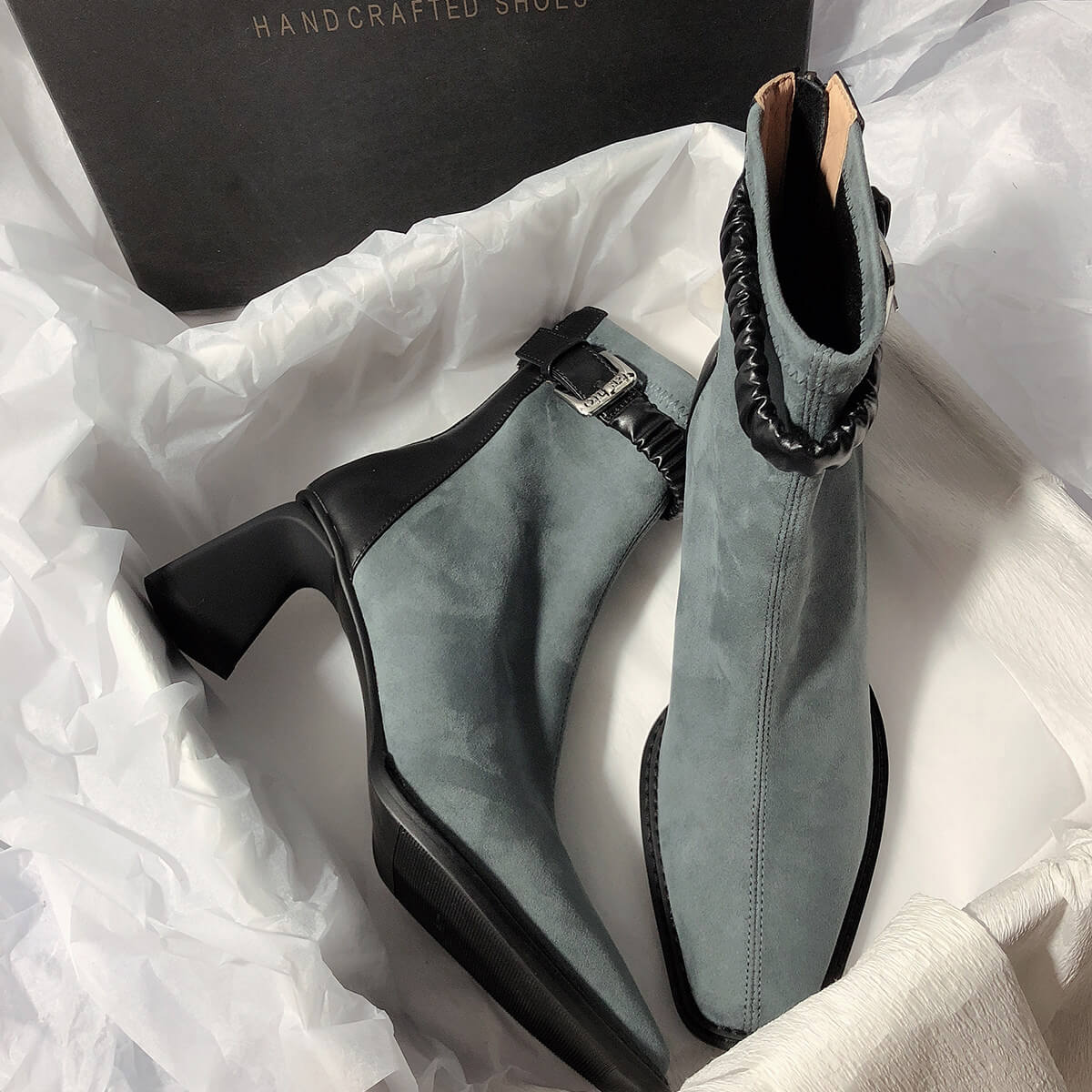 Two grey suede boots arranged inside a "HANDCRAFTED SHOES" box, one showing the side profile and the other showing the front view.