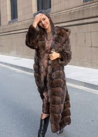 A full-body shot of a woman laughing and adjusting her hair while wearing a long fur coat over a tiger-print dress and black pointed-toe boots.