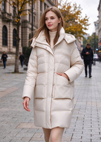 Front walking shot of a woman in an ivory hooded quilted down coat featuring front flap pockets and cozy high neck styling.