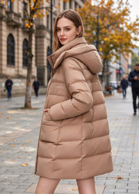 Side-back perspective of a woman wearing a camel beige hooded winter down jacket highlighting cocoon silhouette and quilted baffle construction.
