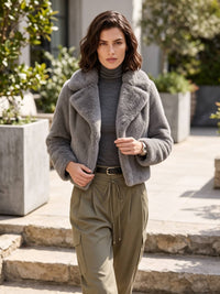 A woman stands on outdoor stone steps wearing a gray fuzzy cropped jacket over a gray turtleneck, olive green drawstring pants, and a black belt.