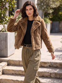 A woman walking outdoors on stone steps wearing a brown fuzzy cropped jacket over a black top and olive cargo pants.