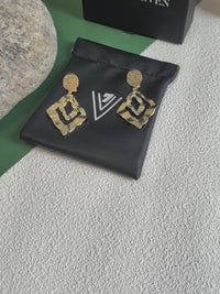 The video highlights the earrings' reflective quality and intricate details by showing them on a black branded pouch and being held up for a close-up view.