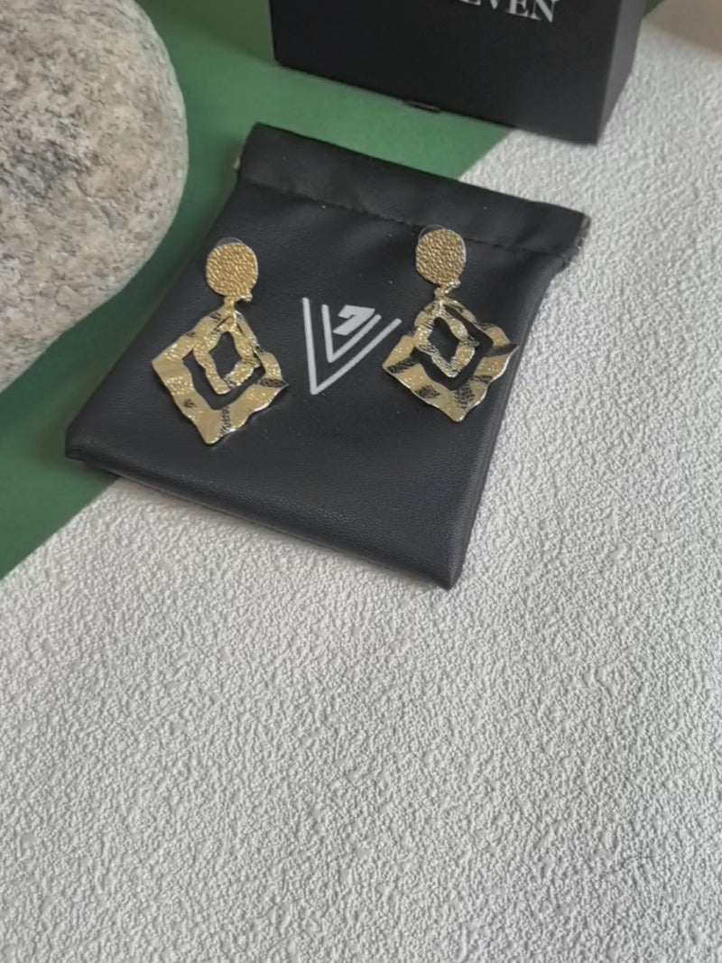 The video highlights the earrings' reflective quality and intricate details by showing them on a black branded pouch and being held up for a close-up view.