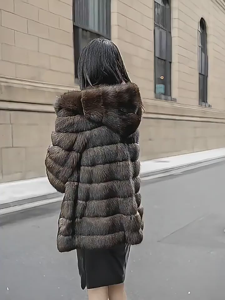 A woman models a luxurious, dark brown faux fur jacket with horizontal panelling and a generous hood. She walks along a city street, showcasing the jacket's plush texture and voluminous sleeves. She styles it with a grey top and a long black leather skirt featuring a thigh-high slit. The video captures her smiling and posing against the backdrop of a classic stone building.